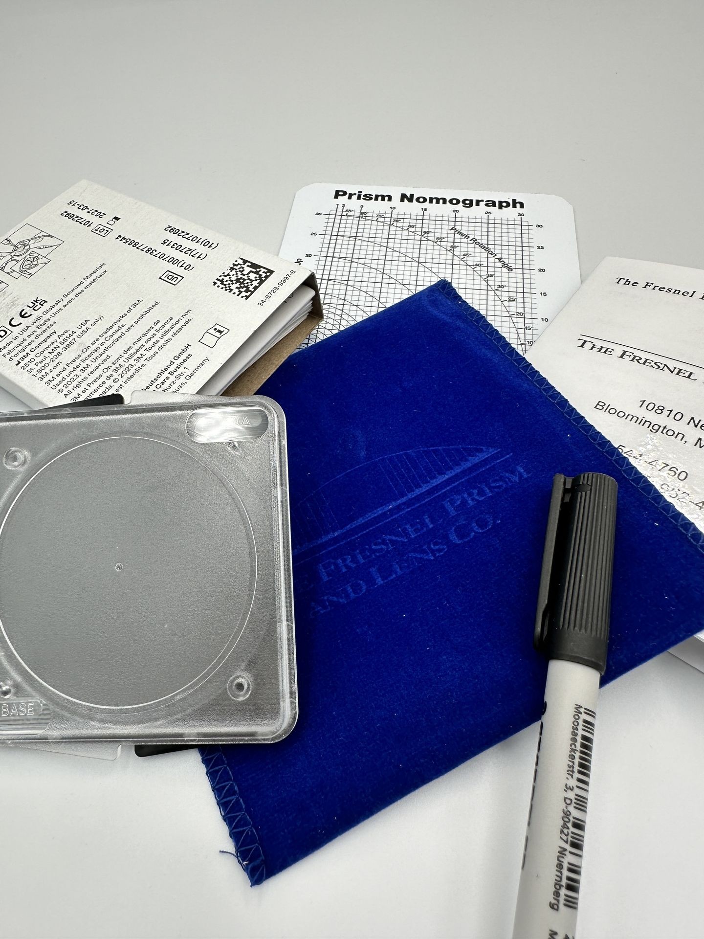 Fresnel prism packaging with graph paper, blue cloth, and pen on a white surface.
